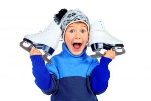 Cheerful little boy in warm sweater and hat holding figure skates. Isolated over white background